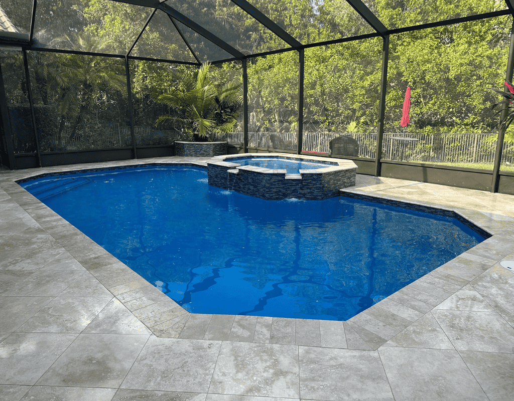 Completed custom-built swimming pool with raised spa, mosaic tile accents and travertine deck inside a screened enclosure by Pools USA in Port St. Lucie, FL.